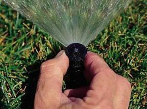 a tech adjusts a pop up sprinkler head by hand